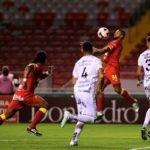 John Jairo Ruiz, delantero de Herediano, detiene el balón con el pecho, ante la mirada de dos defensores manudos.