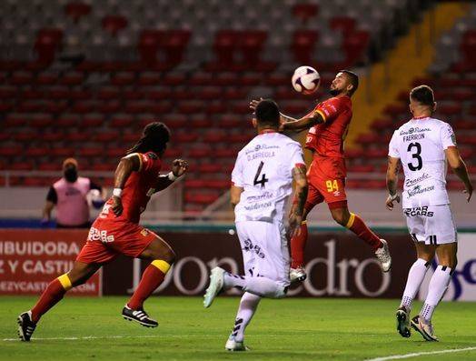 John Jairo Ruiz, delantero de Herediano, detiene el balón con el pecho, ante la mirada de dos defensores manudos.